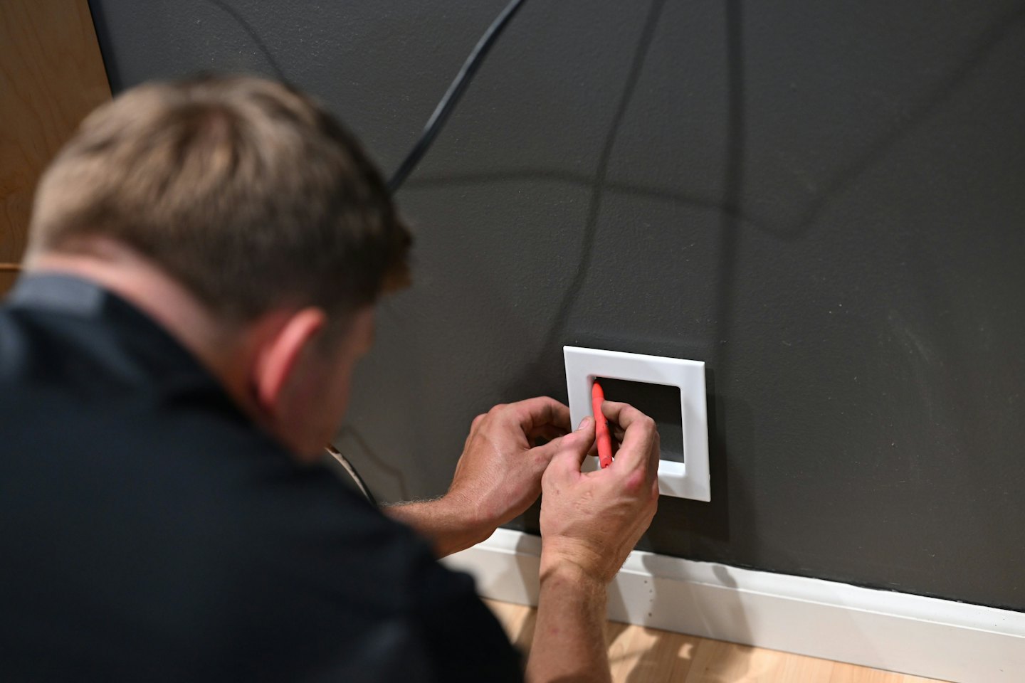 Technician installing a wall plate with a red tool.